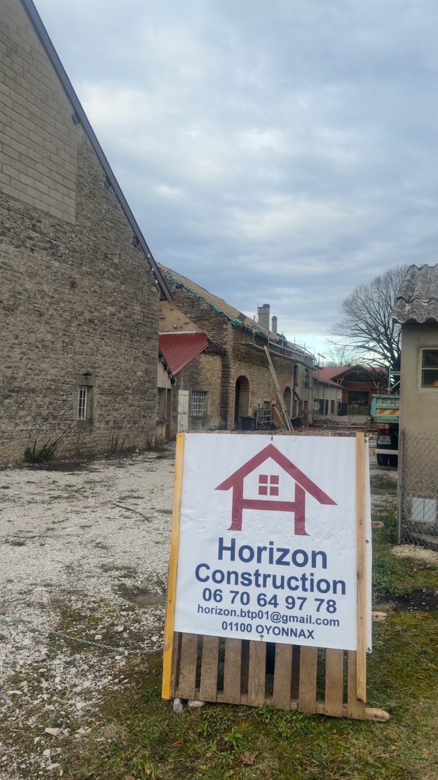 Panneau de chantier Horizon Construction devant une ferme en pierre